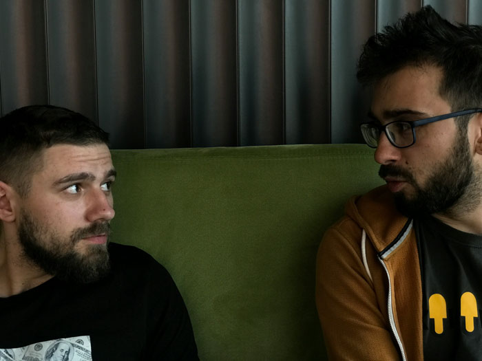 Two men on a couch having a discussion about opening a relationship.