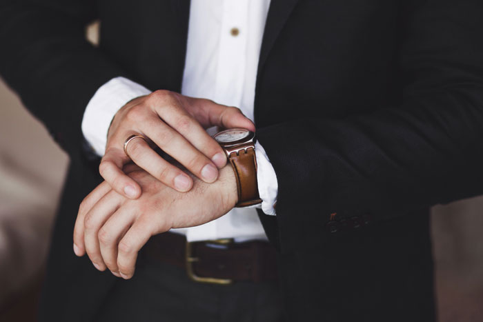 Person in a suit checking time on a wristwatch, symbolizing overlooked problems affecting mental health.