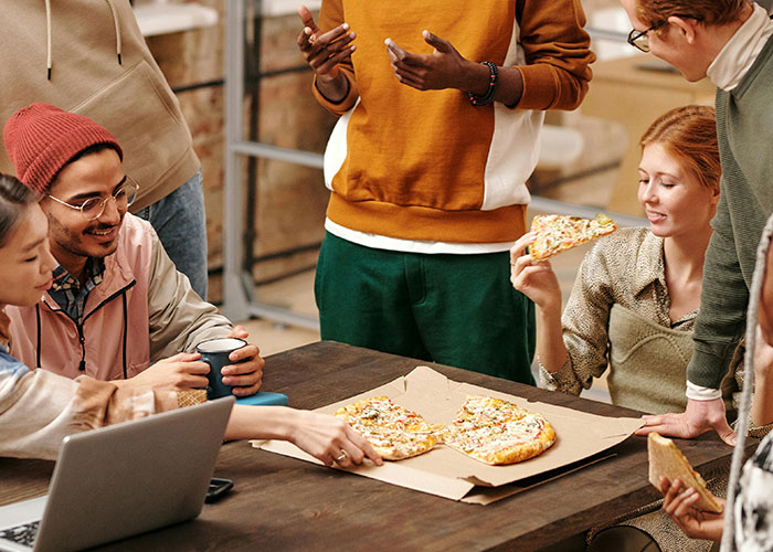 Colleagues enjoying pizza at a workplace, indicating a casual, relaxed office environment.