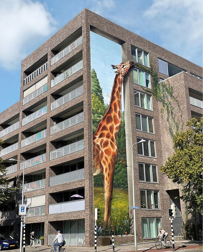 3D street art depicting a giraffe reaching to the top of a building, creating a mind-bending visual effect.