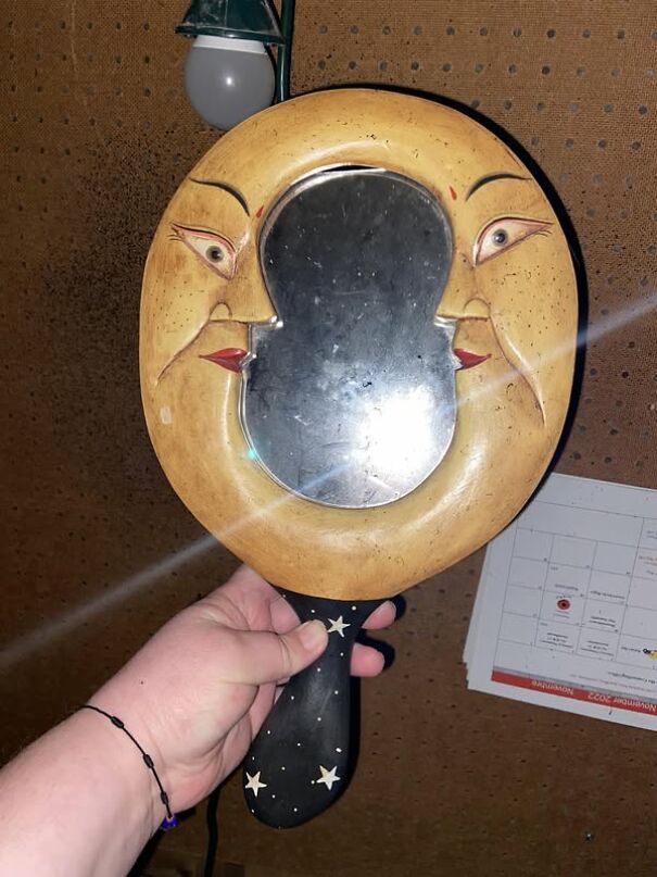 Hand holding a unique moon-themed mirror found while thrifting.