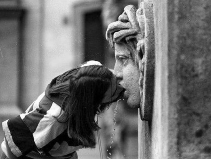 Child drinking from a fountain, creating a perfectly timed street photo of an unexpected optical illusion.