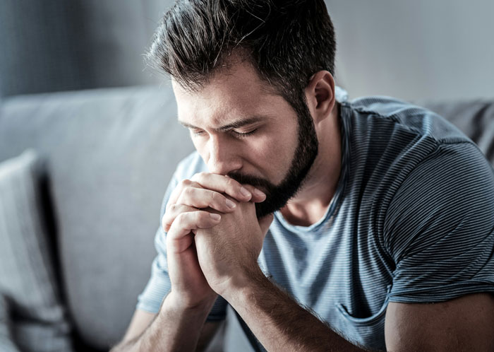 Man contemplating on a sofa, wearing a striped shirt, reflecting on relationship challenges.