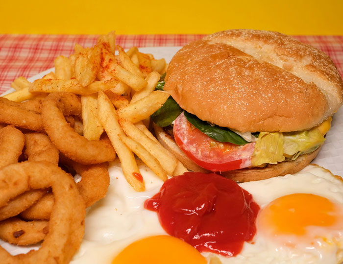 Burger, fries, onion rings, and eggs on a plate exemplify lazy meals shared by people online.