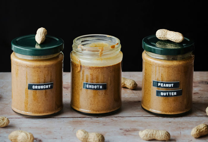 Jars of crunchy and smooth peanut butter with peanuts on a wooden table.