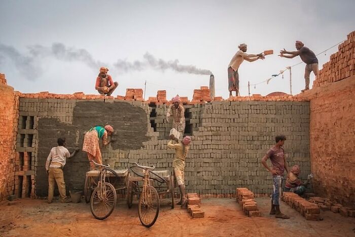 Workers passing bricks on a wall, with smoke visible in the background, capturing unexpected street moments.