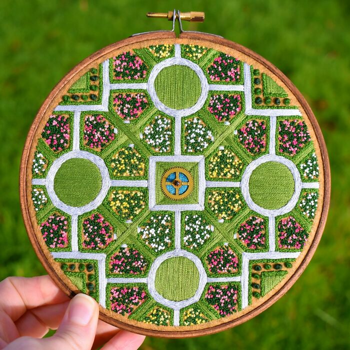 Landscape embroidery with intricate garden design, featuring green grass and colorful flowers on a hoop.