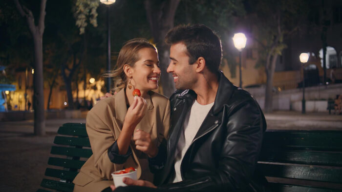 Couple enjoying strawberries on a park bench at night, showcasing green flags on a first date.