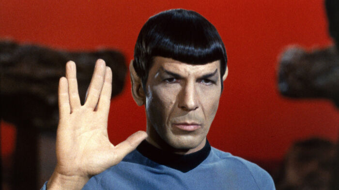 Character in Starfleet uniform performs Vulcan salute with serious expression, symbolizing an iconic role.