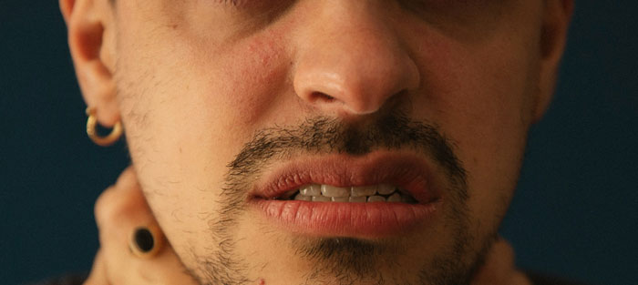 Man with visible burn scars and distressed expression, wearing a gold hoop earring, possibly experiencing a breakup.