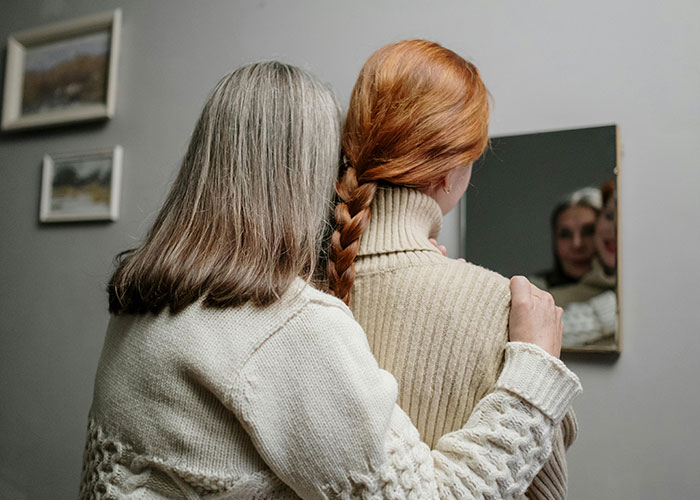 Two people embrace in front of a mirror, capturing a heartfelt reaction after coming out.