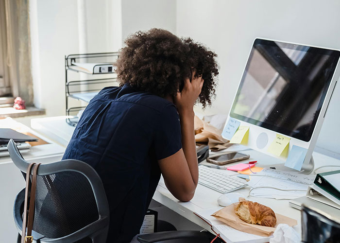Stressed employee at cluttered desk, holding head in hands, showing signs of a toxic workplace.