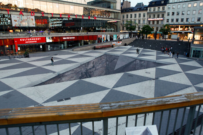3D street art creating an optical illusion of a deep pit in a city square.