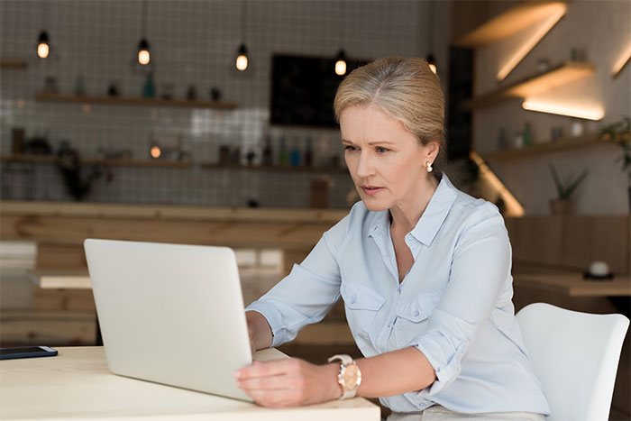 Woman in a light blue shirt concentrating on a laptop, pondering relationship decisions.
