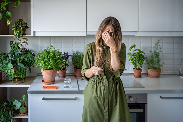 Woman in a green dress stands in a kitchen full of plants, looking distressed. Woman in a green dress stands in a kitchen full of plants, looking distressed.