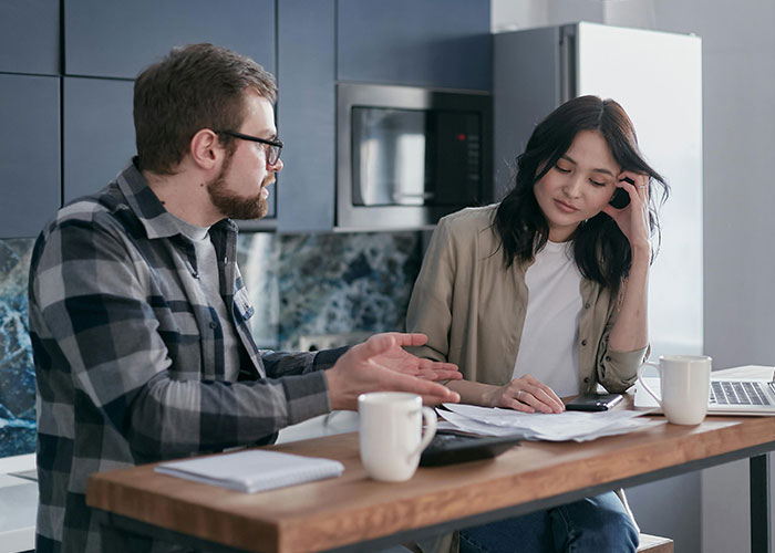 Man discussing property advice with woman at a kitchen table, surrounded by papers and coffee mugs.