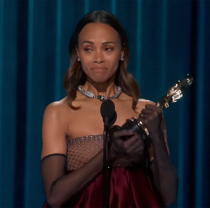 Woman holding an award on stage in a formal dress.