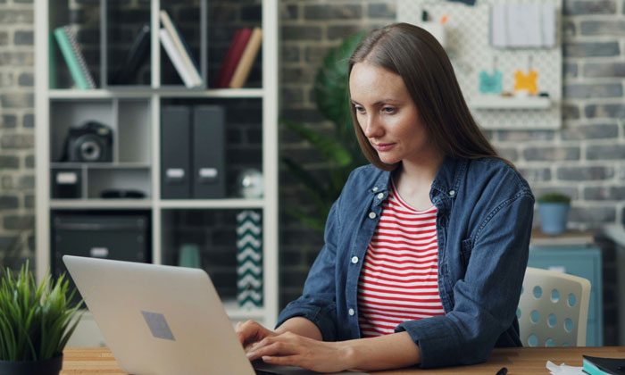 Person in casual wear working on a laptop in a home office, addressing mental health issues.