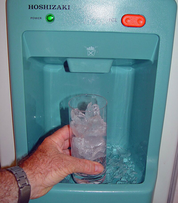 Man filling a glass with ice from a home dispenser, highlighting typical American appliance feature.