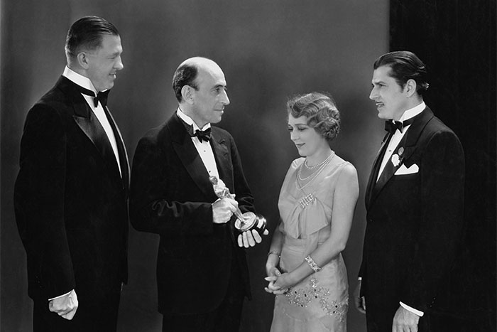 Four individuals in formal attire at an award show, with one holding a statuette, showcasing a classic moment.
