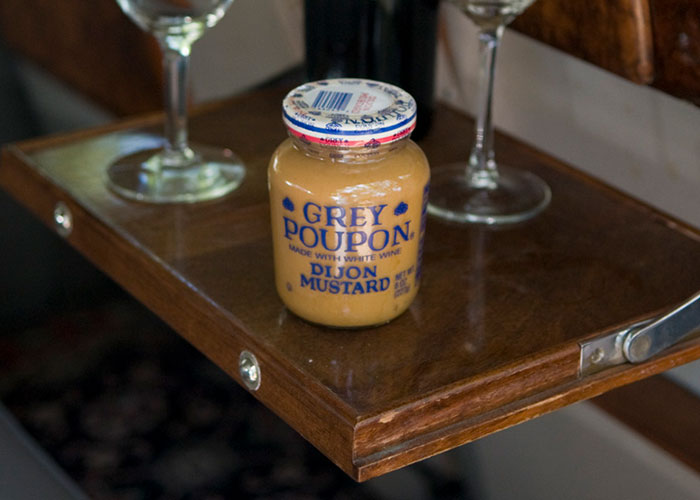 Jar of Grey Poupon Dijon Mustard on a wooden tray with two wine glasses.