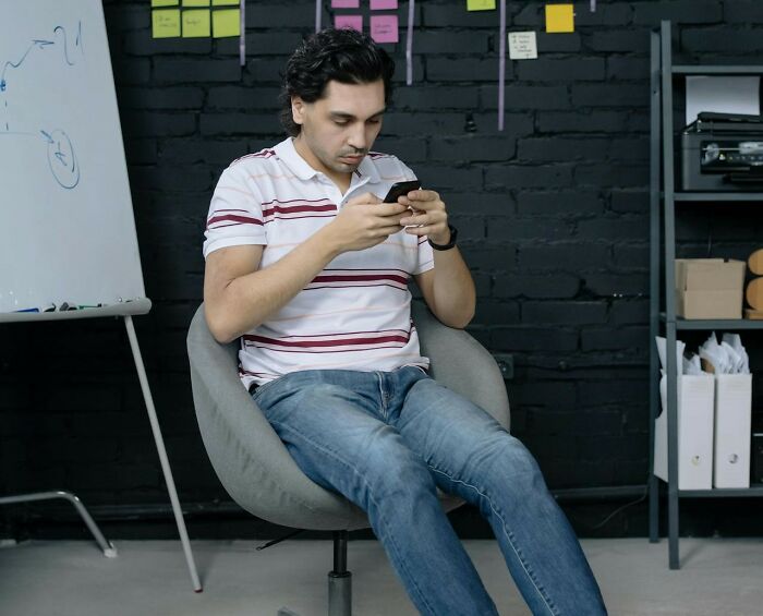 Man distracted on phone during a job interview, wearing casual clothes in an office. Worst interview scenario.
