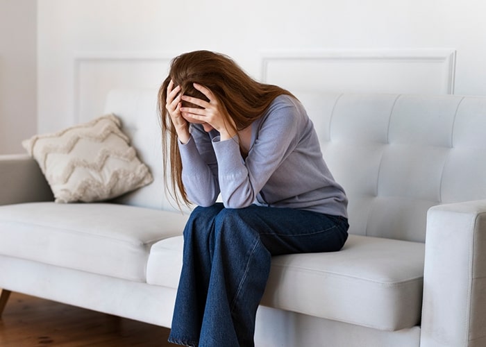 A stressed parent sitting on a couch, head in hands, reflecting on parenting mistakes.