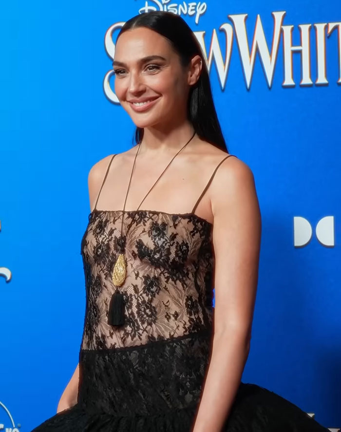 Actress in a black lace dress at a 'Snow White' event, smiling against a blue background.