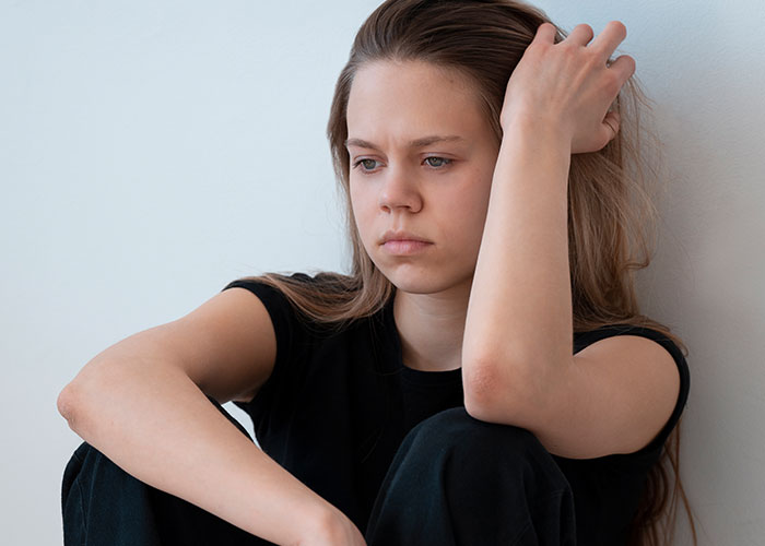 Teen girl sitting pensively with hand in hair, contemplating sweet 16 rules and respect.