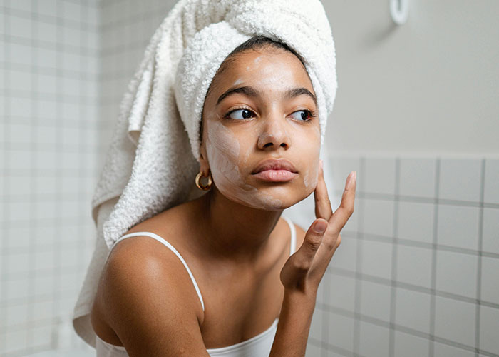 Woman applying face mask, wrapped in a towel, showcasing beauty tips.