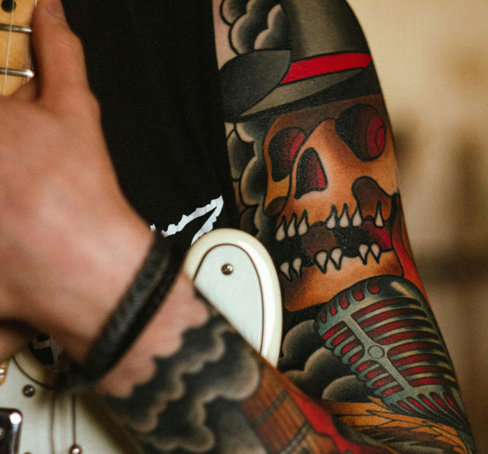 Tattoo of a skull in a hat and vintage microphone on an arm.