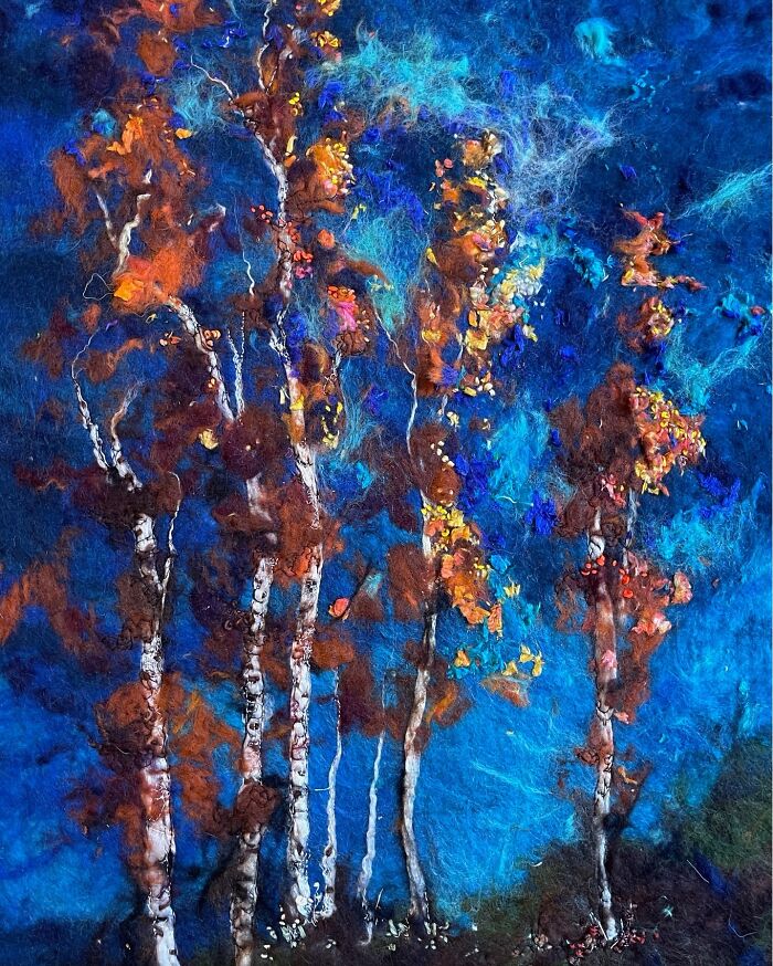 Fiber art depicting a vibrant forest scene with blue and orange hues, created with wool fibers for a textured landscape effect.