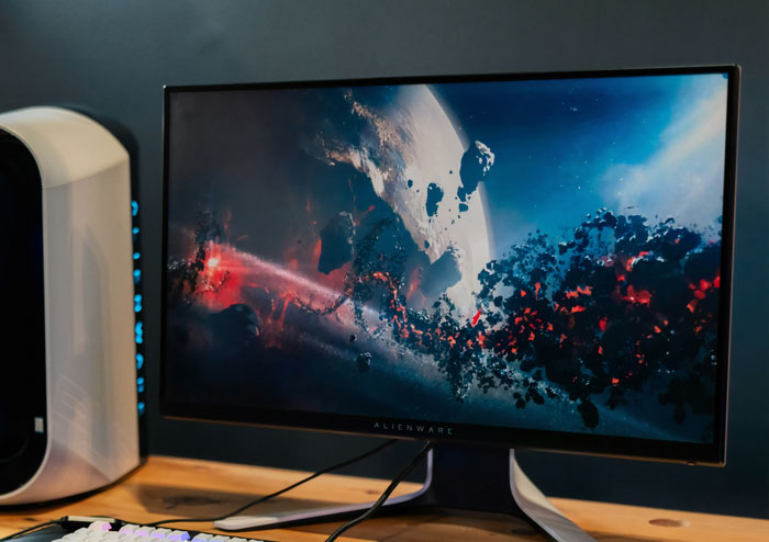 Alienware monitor displaying a space-themed wallpaper; commonly found in home offices for gaming and work.