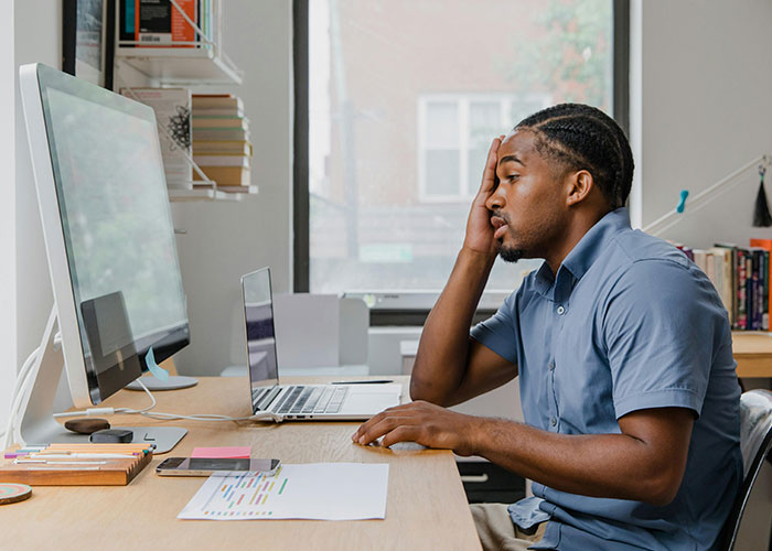 Man in blue shirt at desk, looking stressed, illustrating workplace toxic red flags.