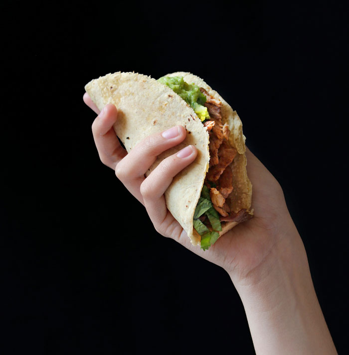 A hand holding a taco filled with lettuce, meat, and guacamole, showcasing a lazy meal idea.