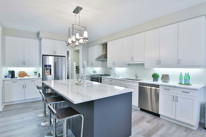 Modern kitchen with a marble island, four stools, stainless steel appliances, and white cabinets, featuring garbage disposal.