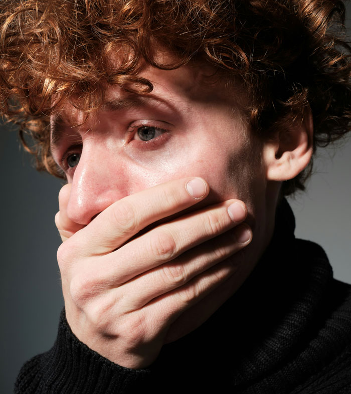 A person with red hair looks distressed, covering their mouth in a shadowed setting, related to breakup assumption and burn scars.