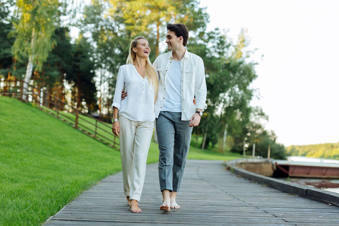 Couple walking on a wooden path, smiling and embracing, illustrating green flags on a first date.