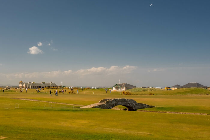Golfers enjoying a round at a breathtaking course with a stone bridge under a clear blue sky.
