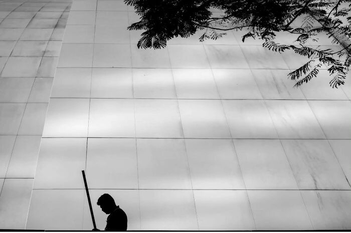 Silhouette of a person with a broom against a large building wall, capturing the raw beauty of street life.