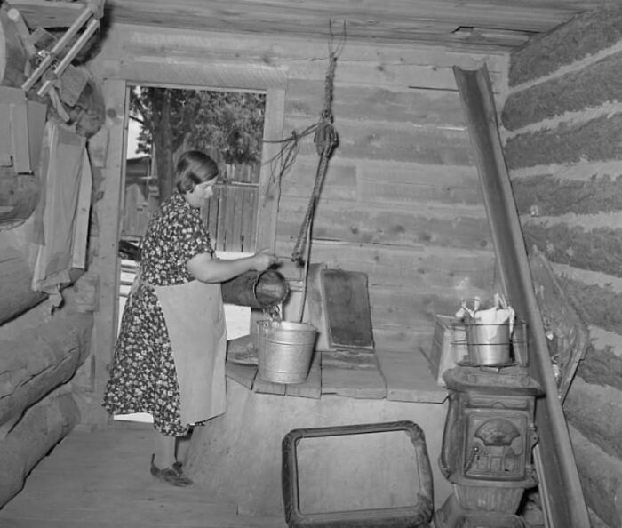 Woman in a rustic kitchen pouring water into a bucket, illustrating a lesser-known historical moment.