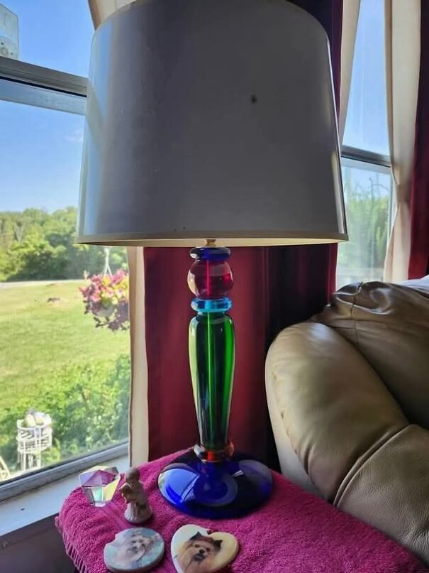 Colorful, unusual lamp with a white shade on a windowsill, next to a couch, showcasing a strange thrifting find.