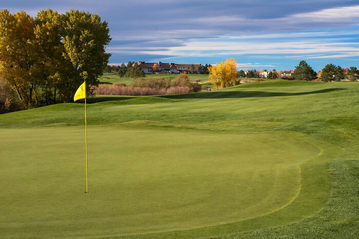 Breathtaking golf course with a lush green, showcasing vibrant trees and distant buildings under a dramatic sky.