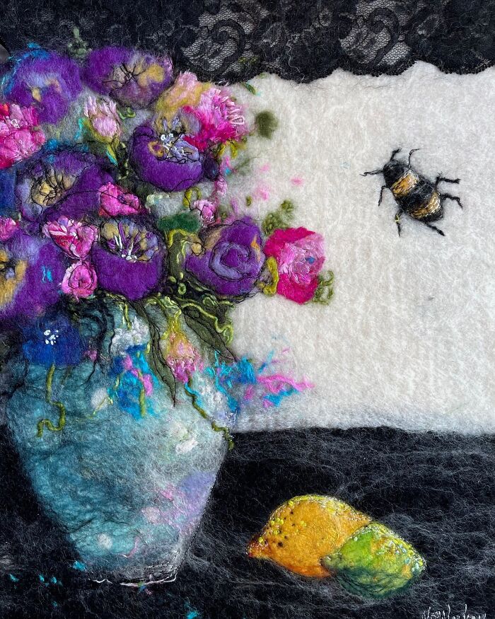Fiber artwork depicting a vibrant bouquet in a vase, a bee, and lemons in a scenic setting.