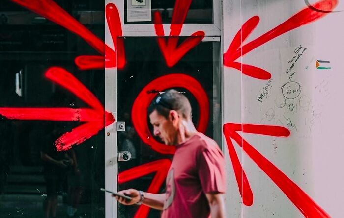 Man walking past street art with red arrows in a perfectly timed photo capturing an unexpected moment.