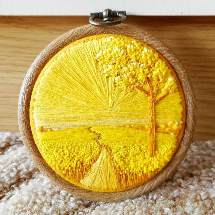 Yellow landscape embroidery art featuring a tree and path in a round wooden frame.