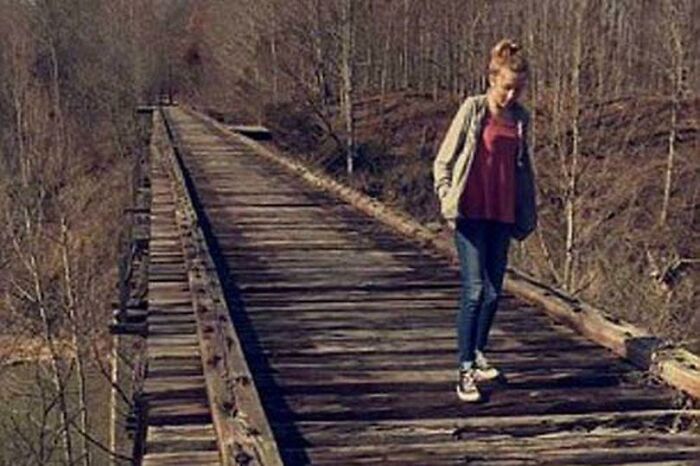 Young woman walking on an abandoned railway bridge in a forest, evoking a creepy and mysterious atmosphere.