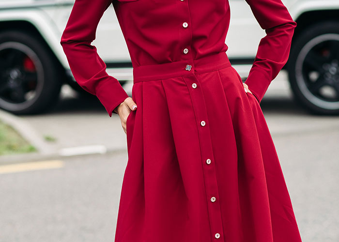 Woman in a red dress stands with hands on hips, in front of a car, emphasizing respect and Sweet 16 theme.