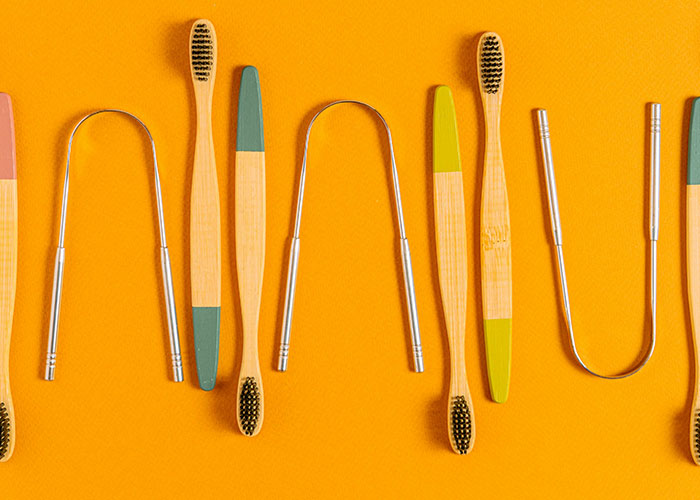 Bamboo toothbrushes and tongue cleaners on an orange background, showcasing beauty tips essentials.