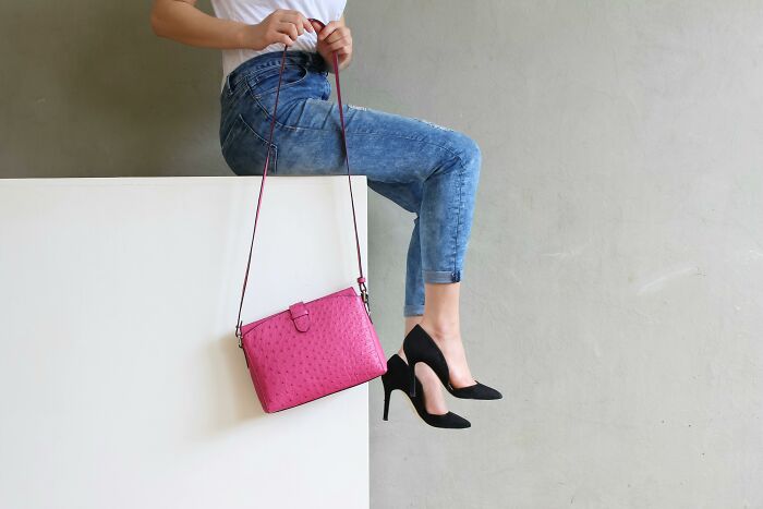 Person in jeans and heels sitting on ledge with pink handbag, suggesting wild theories of style choices.